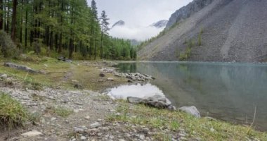 4K UHD dağ gölü zaman ayarlı yaz veya sonbahar saatlerinde. Vahşi doğa ve kırsal dağ vadisi. Çam ağaçlarından oluşan yeşil orman ve gökyüzünde hızlı bulutlar. Motorlu doli kaydırma hareketi