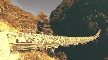 Khumbu vadisindeki en büyük asma köprü renkli Tibet dua bayraklarıyla. Vahşi Himalayalar yüksek irtifa doğa ve dağ vadisi. Ağaçlarla kaplı kayalık yamaçlar. Trek alanı ana kampa gidiyor.