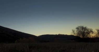 4k dağ çayırı yaz ya da sonbahar gündoğumu saatlerinde zaman atlaması. Vahşi doğa ve kırsal alan. Açık gökyüzü, ağaçlar, yeşil ve sarı çimenler, ufukta güneş ışığı. Motorlu kaydırma hareketi.