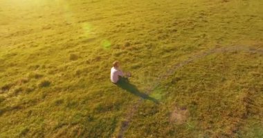 Havadan bakış açısı. Yeşil çimlerin üzerinde oturan, sarı kırsal alanda not defteri olan ve telefonla konuşan bir adam. Günlük kıyafet. Güneş ışınları. Radikal hareket.