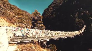 Khumbu vadisindeki en büyük asma köprü renkli Tibet dua bayraklarıyla. Vahşi Himalayalar yüksek irtifa doğa ve dağ vadisi. Ağaçlarla kaplı kayalık yamaçlar. Trek alanı ana kampa gidiyor.