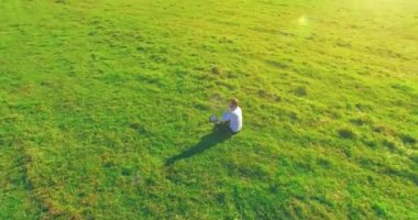 Havadan bakış açısı. Yeşil çimlerin üzerinde oturan, sarı kırsal alanda not defteri olan ve telefonla konuşan bir adam. Günlük kıyafet. Güneş ışınları. Radikal hareket.