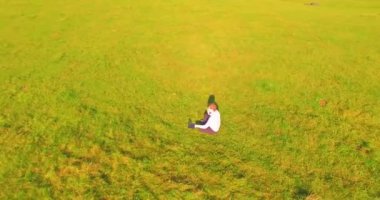 Havadan bakış açısı. Yeşil çimlerin üzerinde oturan, sarı kırsal alanda not defteri olan ve telefonla konuşan bir adam. Günlük kıyafet. Güneş ışınları. Radikal hareket.