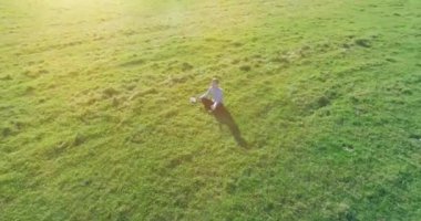 Havadan bakış açısı. Yeşil çimlerde oturan ve kırsal alanda not defteri olan bir adamın etrafında alçak yörünge uçuşları. Günlük giysi ve zen meditasyon pozu. Güneş ışınları. Radikal hareket.