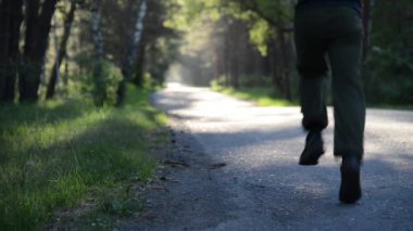 Yeni asfalt yolda koşan FHD sporcusu. Şehir parkında gün doğumu ya da gün batımı. Yeşil ağaç ormanı ve ufukta güneş ışınları. Düz renk.