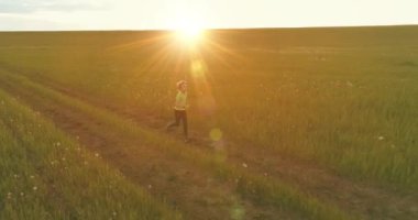 Sportif bir çocuğun havadan çekimleri buğday tarlasından geçiyor. Kırsal çayırlarda akşam sporu alıştırmaları. Mutlu bir çocukluk sağlıklı bir yaşam biçimidir. Açık havada koşma transferi. Radikal hareket, güneş