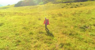 Hava 4K UHD görüntüsü. Yeşil dağ tarlasında yürüyen genç turist üzerinde alçak irtifa uçuşu. Büyük bir kırsal vadi ve yaz günü güneşli bir çayır. Sırt çantalı gezgin..