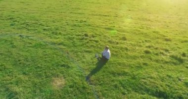 Havadan bakış açısı. Yeşil çimlerin üzerinde oturan, sarı kırsal alanda not defteri olan ve telefonla konuşan bir adam. Günlük kıyafet. Güneş ışınları. Radikal hareket.