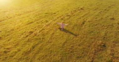 Havadan bakış açısı. Yeşil çimlerde oturan ve kırsal alanda not defteri olan bir adamın etrafında alçak yörünge uçuşları. Gündelik kıyafet ve Zen meditasyonu. Eller havada. Güneş ışınları. Radikal hareket.
