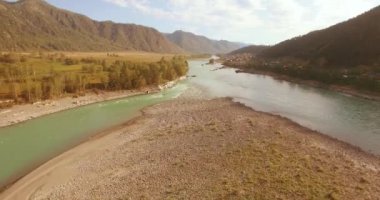 4K hava bakış açısı. Güneşli yaz sabahında, taze, hızlı dağ nehri üzerinde kayalıklarla alçak irtifa uçuşu. Yeşil çam ağaçları ve güneş ışınları. Saf soğuk su akıntısı.