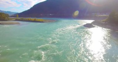 4K hava bakış açısı. Güneşli yaz sabahında, taze, hızlı dağ nehri üzerinde kayalıklarla alçak irtifa uçuşu. Yeşil çam ağaçları ve güneş ışınları. Saf soğuk su akıntısı.