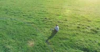 Havadan bakış açısı. Yeşil çimlerin üzerinde oturan, sarı kırsal alanda not defteri olan ve telefonla konuşan bir adam. Günlük kıyafet. Güneş ışınları. Radikal hareket.
