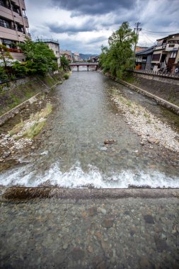 Arka planda tahta bir köprü olan bir nehrin dikey görüntüsü.