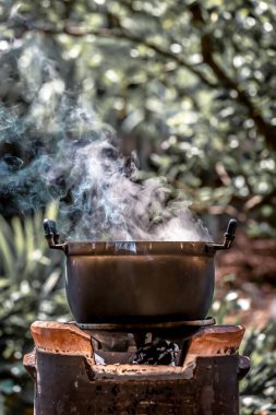 Ormanda ateşte kazan pişirmek, arka planda duman çıkarmak. Yangında kazan pişirmek