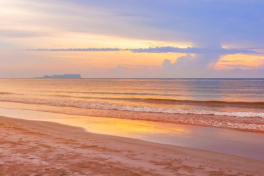 Sahilde gün doğumu, arkada deniz ve tropikal plaj var.