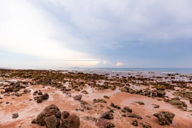 Bulutlu bir gökyüzü ve arka planda bulutlu bir gökyüzü olan kayalık bir sahilin alçak açılı görüntüsü.