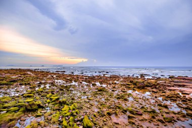 Gökyüzünde renkli bulutlarla kumsalda gün batımı.