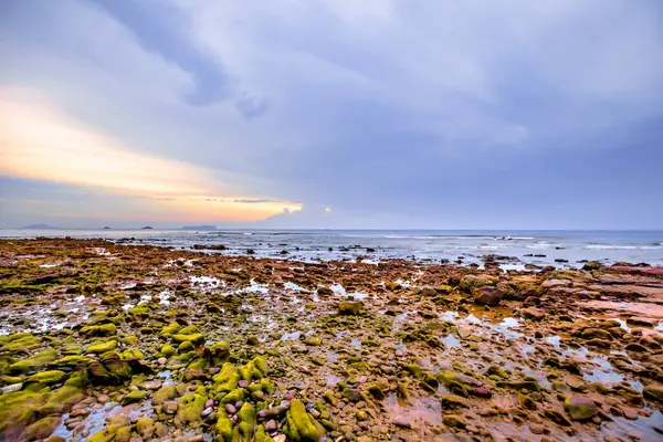 Gökyüzünde renkli bulutlarla kumsalda gün batımı.