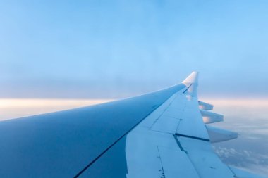 Bulutların üzerinde uçan bir uçağın kanadı. Penceresi ve güneşi olan beyaz bir pencerenin altından manzara. Özgürlük kavramı,