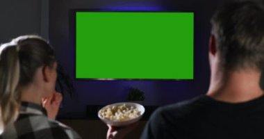 Genç bir çift evde kanepede oturup patlamış mısır yiyor ve televizyon seyrediyor. Film gecesi. boş yeşil ekran