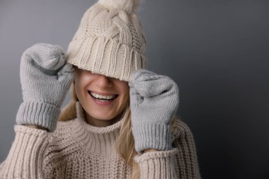 Gülümseyen neşeli kadın yün şapkanın altında yüzünü gizliyor. Moda kışı kıyafetleri