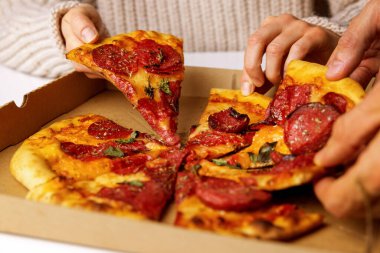 Eller kutudan pepperoni pizza dilimleri alıyor.