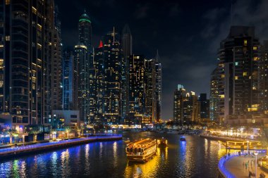 Dubai Marina şehri geceleri ışıklandırılmış gökdelenler ve kanallarda tekneler. BAE