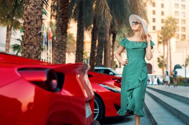 fashion woman in green dress walk Dubai city streets. stands next to luxury sport cars. Arab Emirates travel