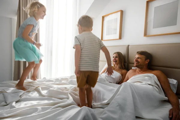 自宅で家族の朝 幸せな子供たちが両親の寝室でベッドに飛び乗り — ストック写真