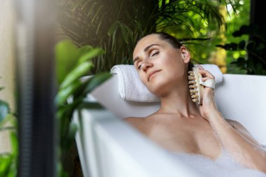 Kadın masaj fırçasıyla sağlık spa banyosunun keyfini çıkarıyor.