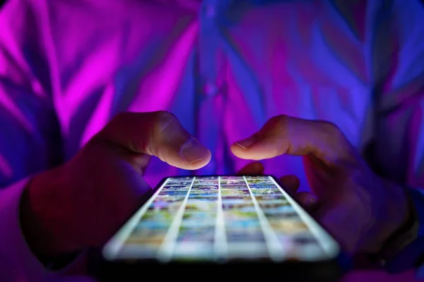 男人用霓虹灯在黑暗的房间里滚动手机屏幕 互联网浏览 社交媒体和营销 — 图库照片