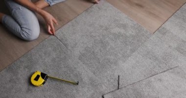 Kadın oturma odasında yere halı döşemesi seriyor. Diy ev geliştirme