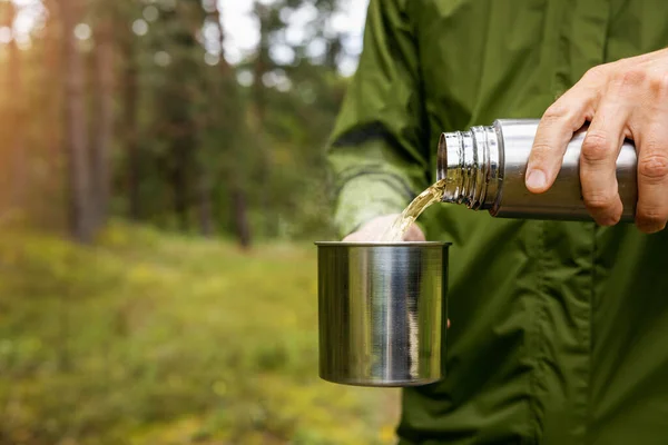 人类把热饮从热水瓶倒进森林里的金属杯子里 自然旅游和露营用具的概念 复制空间 — 图库照片