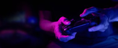 Oyuncuların elinde neon ışıklarda kablosuz video oyun kontrolörüne yakın çekim. Kopyalama alanı olan pankart