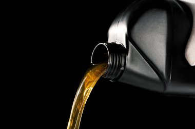 Şişeden araba motoruna yeni motor yağı dökülüyor. Siyah arkaplanda izole