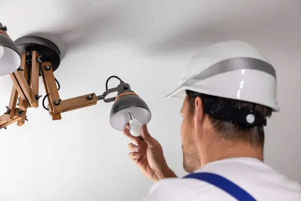 ハンドマンサービス 電気技師は家の天井ランプの導かれた電球を取り替えます ロイヤリティフリーのストック写真