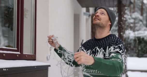 Man Outdoors Christmas Sweater Untangling String Lights House Exterior Decoration — Stock Video
