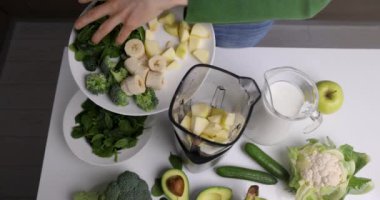 Kadın ev mutfağında sağlıklı vitamin içeceği yapmak için taze sebze ve meyve karıştırıcısına koyar.