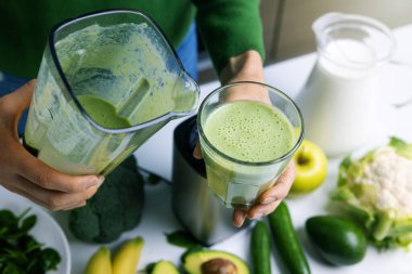 Kadın sebze ve meyvelerden yapılmış bir bardağa taze yeşil meyve suyu dolduruyor. sağlıklı yaşam tarzı