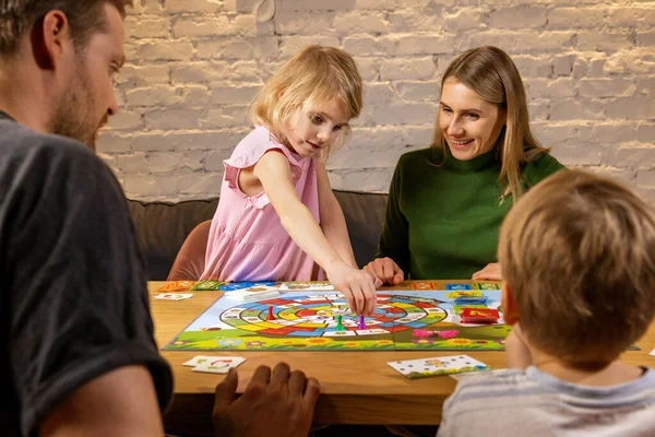 有两个孩子的家庭在一起消磨时光 在家里坐在桌旁玩棋盘游戏 家庭时间 图库图片