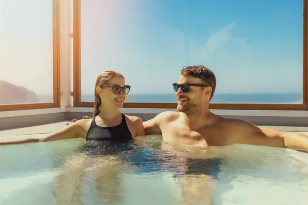 在阳光灿烂的日子 一对情侣在屋顶的按摩浴缸里放松一下 免版税图库图片