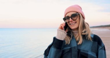 Serin bir günde kumsalda yürürken cep telefonuyla konuşan çekici bir kadın.