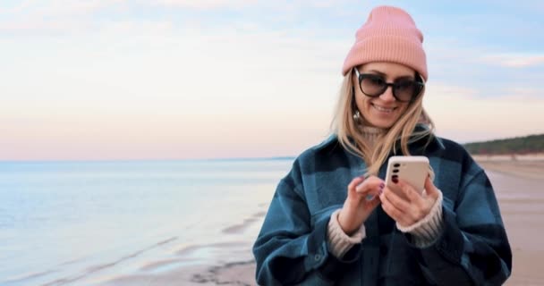 Mujer Sonriente Usando Teléfono Móvil Mientras Camina Costa Playa — Vídeos de Stock