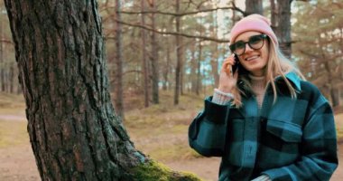 Ormandaki çam ağacının gövdesinde otururken cep telefonuyla konuşan çekici genç bir kadın.