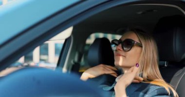 Çekici sarışın kadın arabada oturuyor ve güneş güneşliği aynasına bakıyor. Saç ve güneş gözlüklerini ayarlamak için.