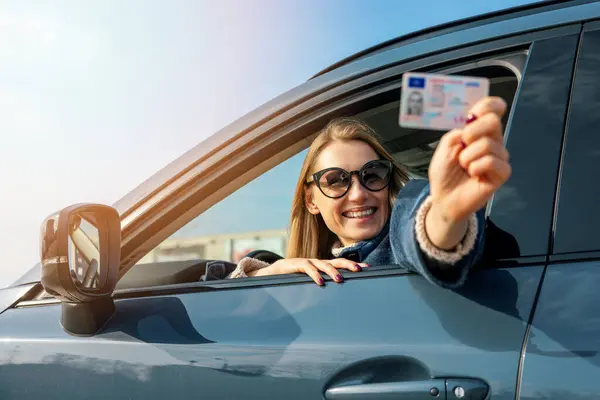晴れた日の車窓から彼女の新しい運転免許証を示す幸せな女性 ストック画像