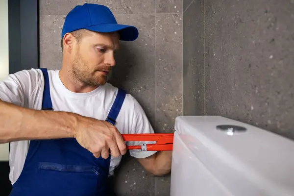 在浴室里工作的管道工用扳手安装水箱管 图库照片