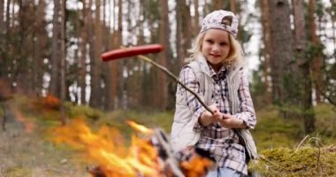 Küçük kız ormanda şenlik ateşinde sosis kızartıyor. Açık hava maceraları