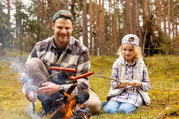 父亲和女儿在森林露营时 一起在篝火边煎香肠 联合活动 免版税图库照片