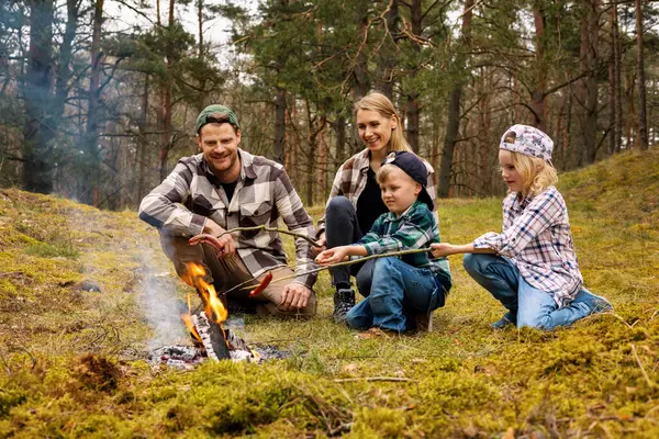 森でキャンプしている間 ボンファイアの上にソーセージを揚げる2人の子供を持つ家族 家族の時間 自然の冒険 ロイヤリティフリーのストック画像